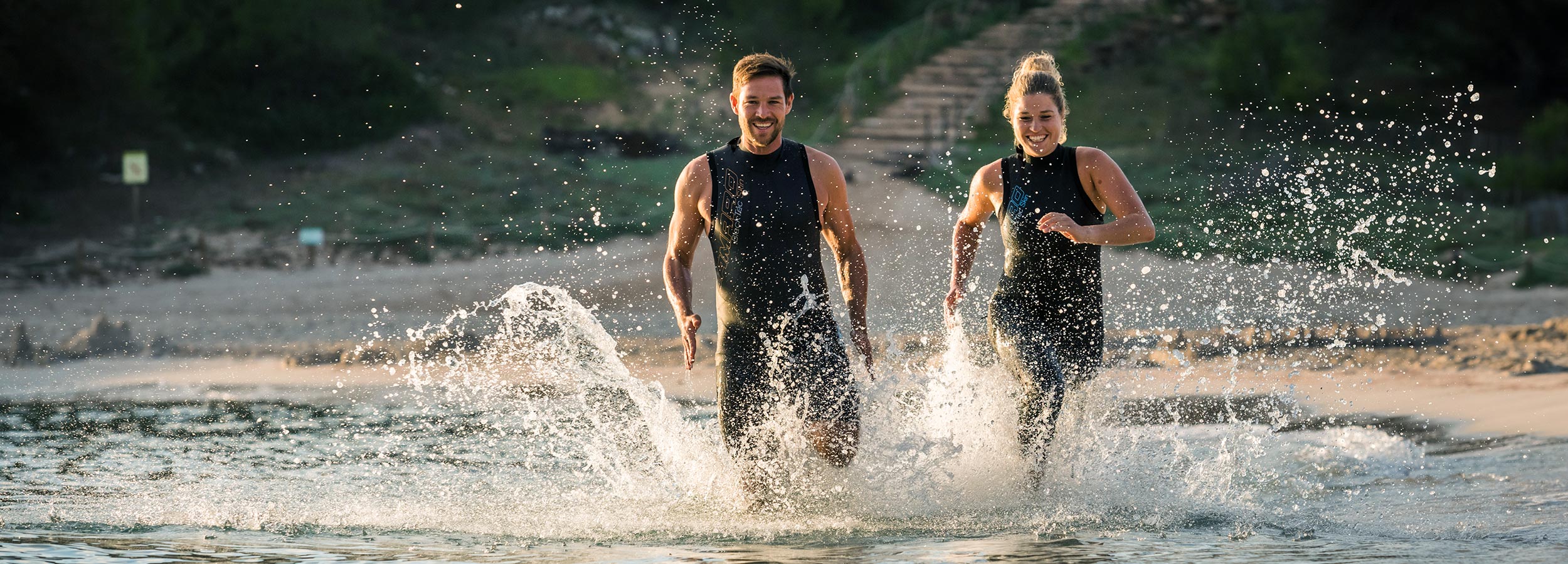 Man and woman running in the water wearing camaro suits
